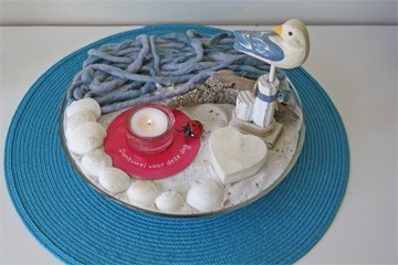 Kijktafel Buitenkans, met zee en strand, zeemeeuw, doosje en lichtje op roze onderzetter Kijktafel Buitenkans, met zee en strand, zeemeeuw, doosje en lichtje op roze onderzetter